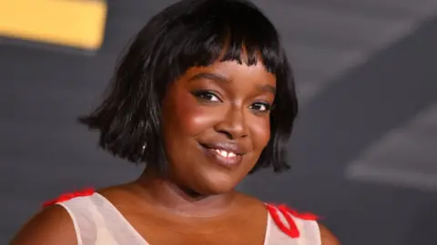 Getty Images British actress Ololade "Lolly" Adefope attends the LA premiere of HBO's original series The Franchise at the Paramount theatre in Los Angeles in October. She is wearing a white and red sleeveless dress.