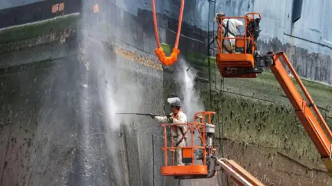 Getty Images Workers clean the hull of a large ship with pressure hoses