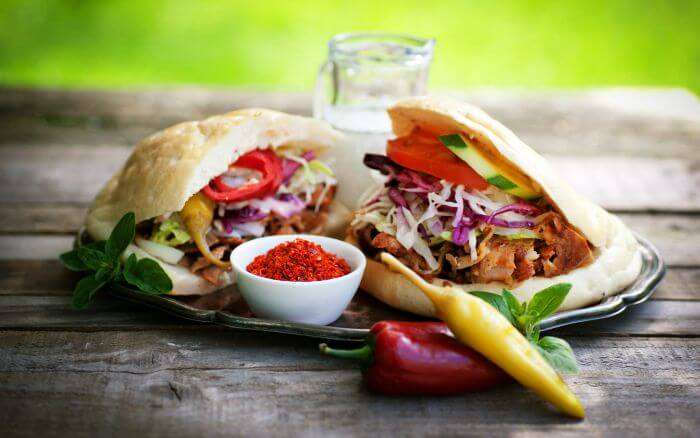 Turkish doner kebab sandwiches filled with spiced meat, fresh vegetables, and served with a side of chili powder