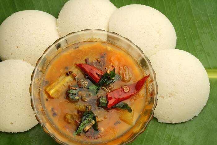 Soft South Indian Idlis served with a bowl of spicy sambar garnished with curry leaves and red chilies on a banana leaf