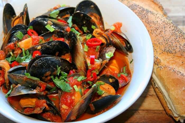 Kallumakkaya Ularthiyathu, Kerala-style mussel stir-fry cooked with spices, garnished with fresh herbs and chilies, served with bread.