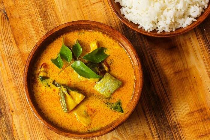 Kerala-style Karimeen Pollichathu, grilled pearl spot fish served on a banana leaf with sliced tomatoes, onions, and green chilies