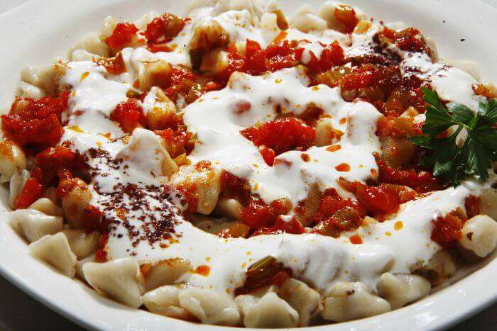 Turkish manti topped with yogurt, tomato sauce, and spices on a plate