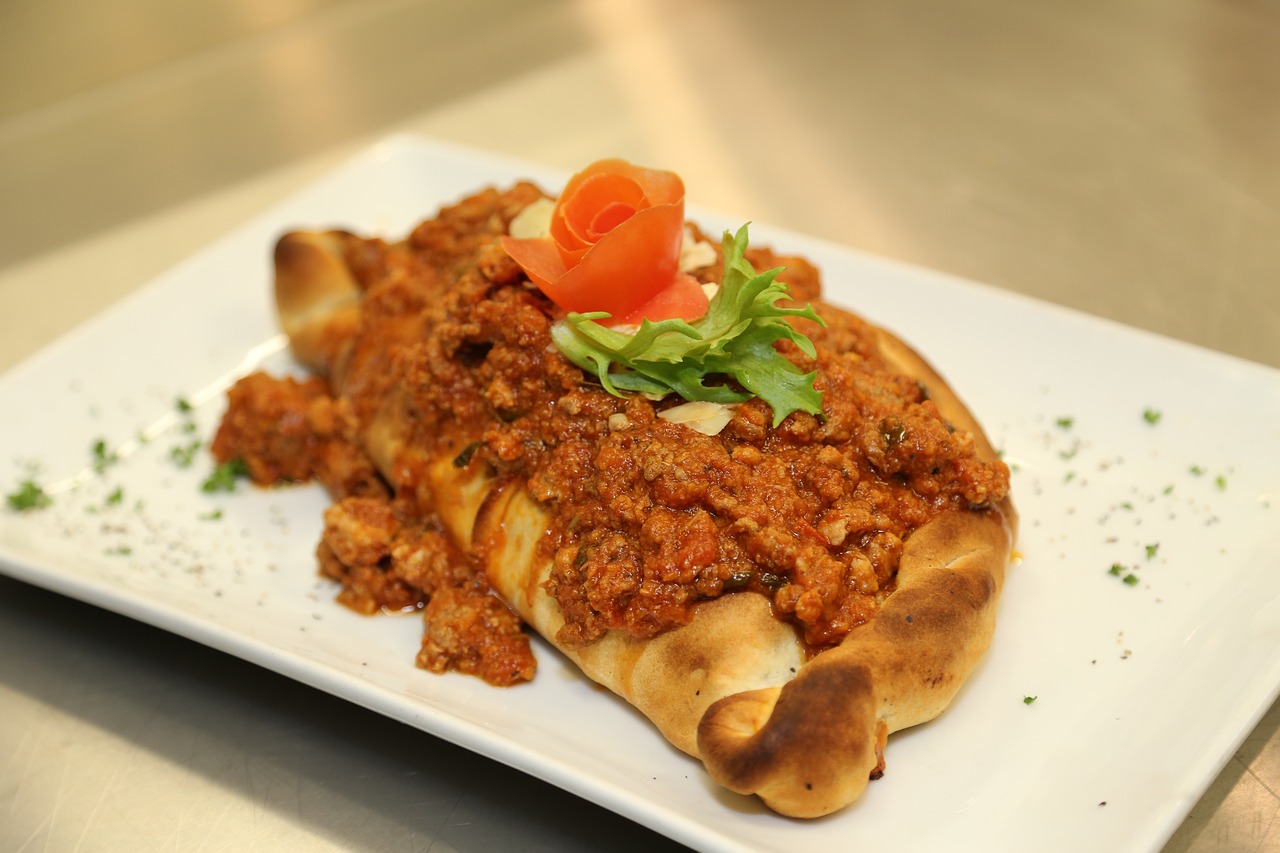 A Turkish pide topped with minced meat sauce and garnished with a tomato rose and fresh greens