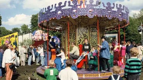 © Keith Haring Foundation/licensed by Artestar, New York. Photo: © Sabina Sarnitz. Courtesy Luna Luna, LLC Children and adults pile onto Keith Haring’s carousel in Hamburg as others watch on.